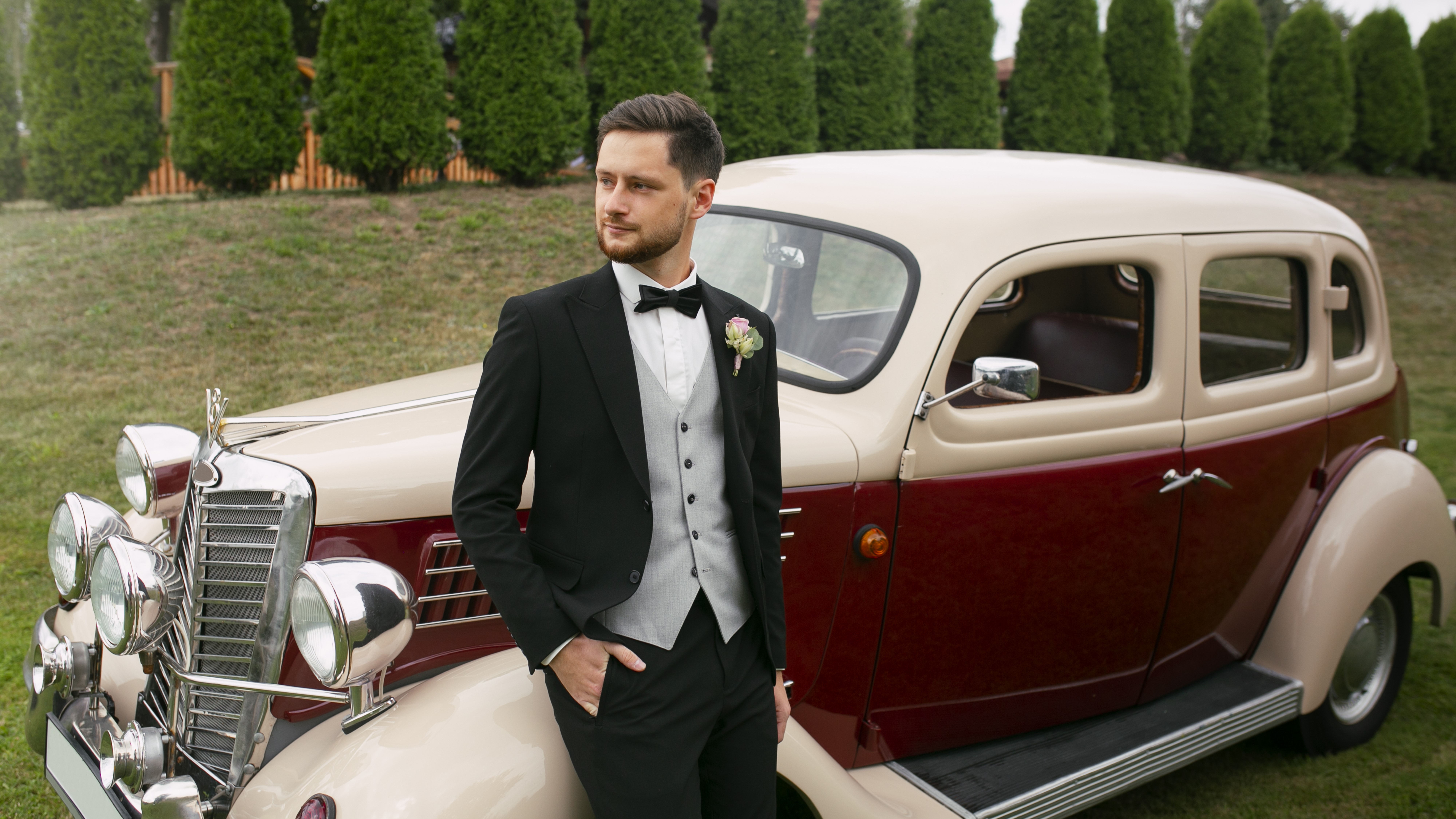 Chauffeur in formal attire standing beside a classic vintage car